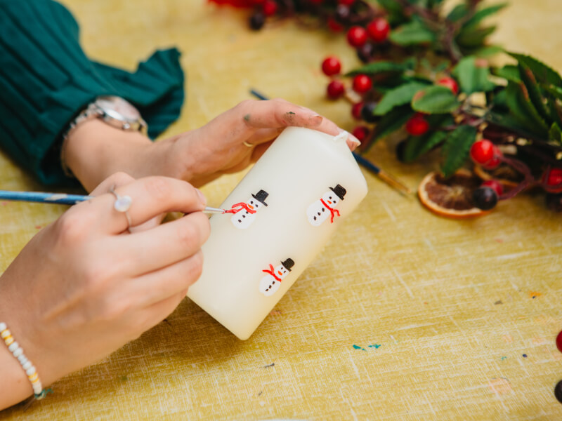 Hand painting snowmen on a candle